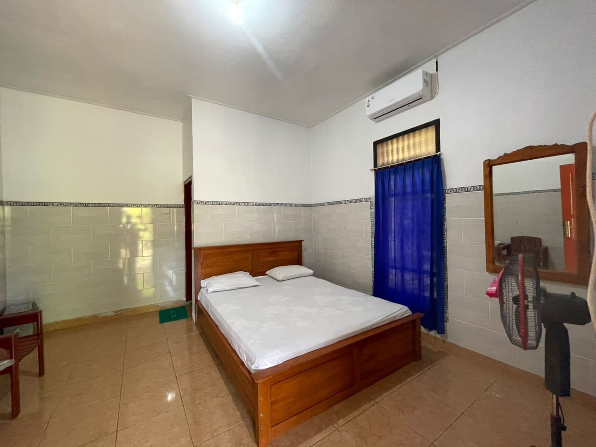 A bedroom with a wooden bed, a ceiling fan, a mirror, and a window with blue curtains.