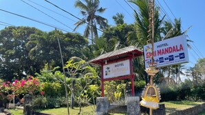 A hotel sign with amenities listed, surrounded by lush greenery and a clear sky. - OYO 95369 Hotel Sari Mandala (Negara)