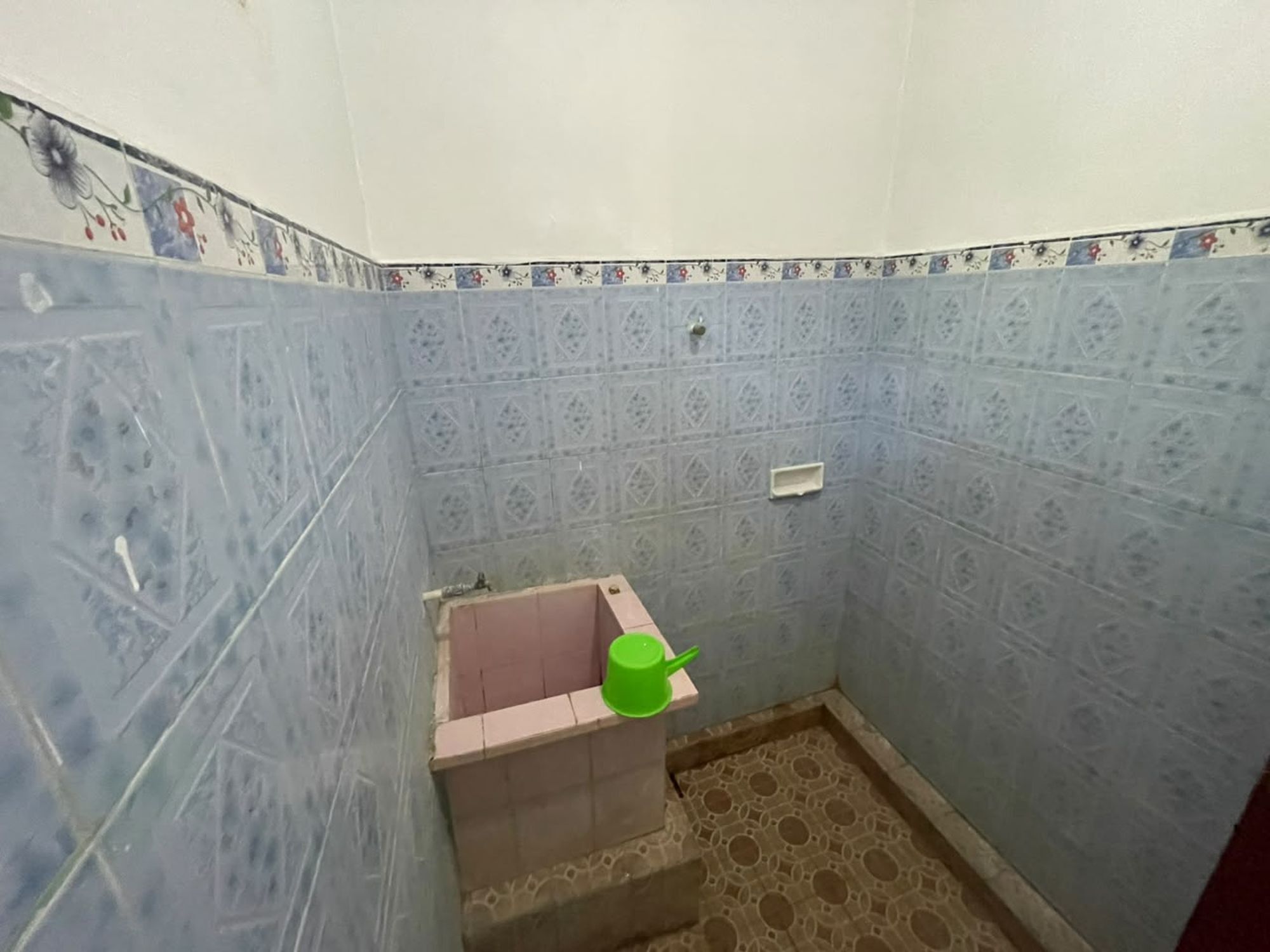 Un baño pequeño con baldosas azules estampadas, un lavabo rosa y una taza verde.