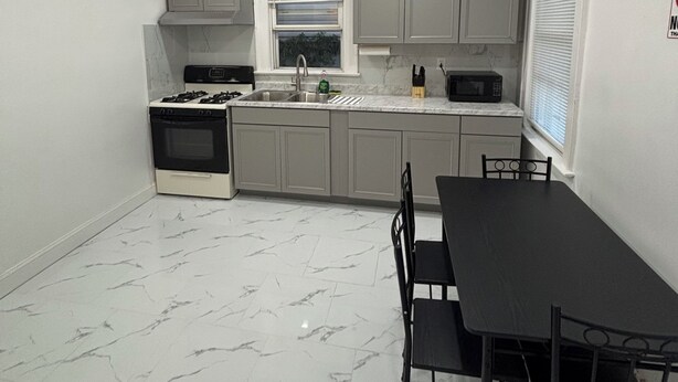 A compact kitchen with a gas stove, sink, and a dining area with a table and chairs. - Modern 2-bedroom apartment near Airport (Newark)