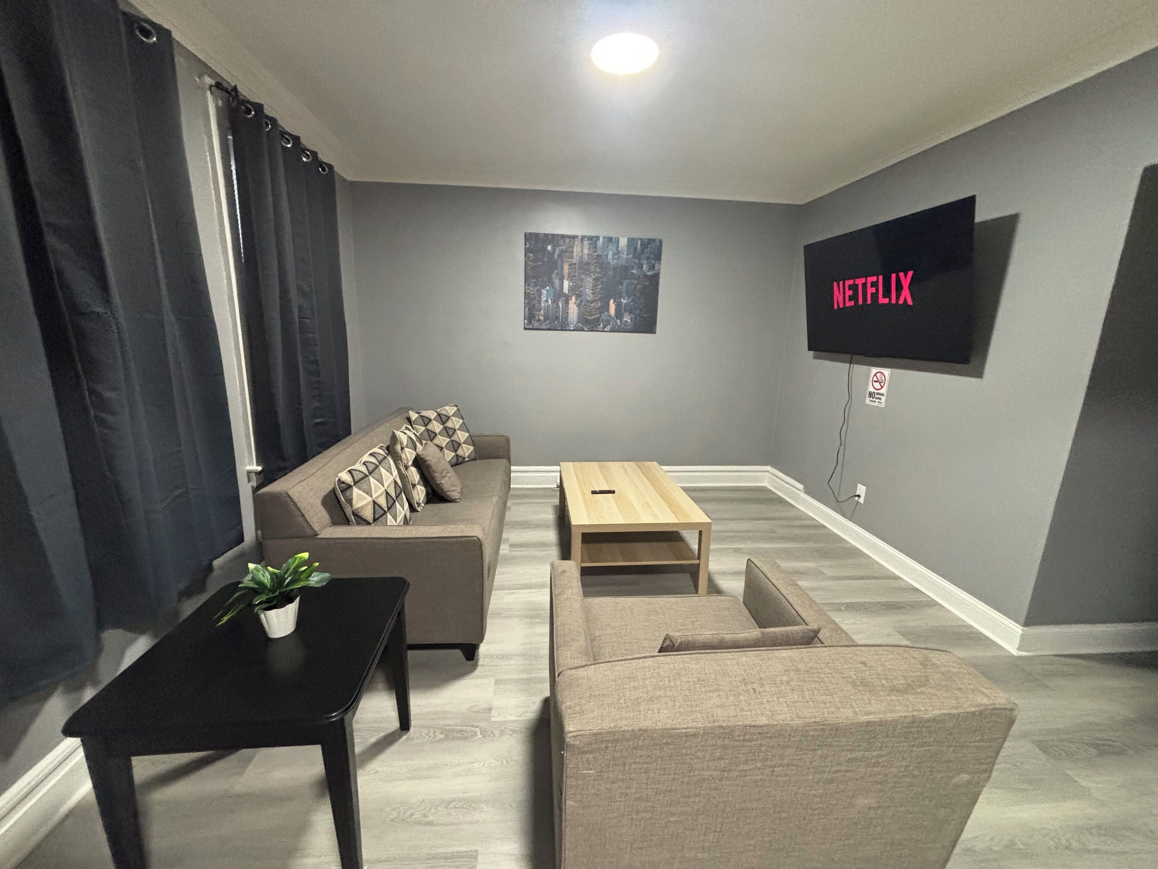 Ein Wohnzimmer mit einer Couch, einem Couchtisch, einem an der Wand montierten Fernseher und einer Pflanze auf einem Beistelltisch.