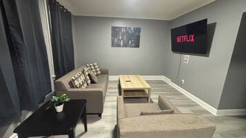 Ein Wohnzimmer mit einer Couch, einem Couchtisch, einem an der Wand montierten Fernseher und einer Pflanze auf einem Beistelltisch.