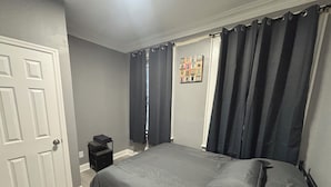 A bedroom with a bed, a nightstand, a door, and a window with curtains. - Modern 2-bedroom apartment near Airport (Newark)