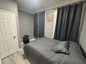 A bedroom with a bed, a nightstand, a door, and a window with curtains.