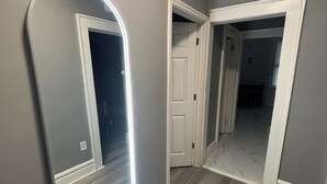 A hallway with a large mirror, a door, and a light fixture. - Modern 2-bedroom apartment near Airport (Newark)