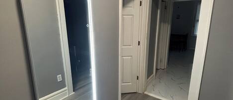 A hallway with a large mirror, a door, and a light fixture.