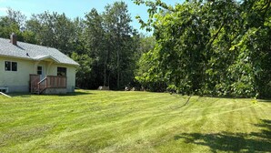 A residential property with a well-maintained lawn, a single-story house with a porch, and a large tree providing shade.