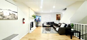 A modern living room with a fireplace, a flat-screen TV, a sofa, and a coffee table. - Cozy 4BR Retreat | Entire House | King Bed | Airport | Ring Road | Games | Banff (Calgary)