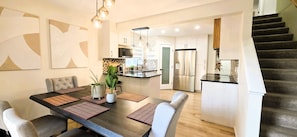 A modern kitchen with a central island, stainless steel appliances, and a staircase leading to an upper level. - Cozy 4BR Retreat | Entire House | King Bed | Airport | Ring Road | Games | Banff (Calgary)