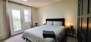 A bedroom with a bed, bedside lamps, a window with curtains, and a door. - Cozy 4BR Retreat | Entire House | King Bed | Airport | Ring Road | Games | Banff (Calgary)