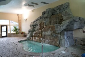 Ein Poolbereich im Innenbereich mit einer Felswand, einem Whirlpool und einem gefliesten Boden.