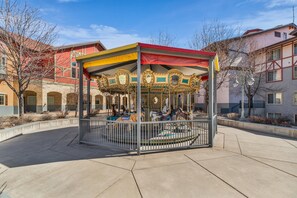 A carousel with ornate golden horses, enclosed by a metal fence, set in a plaza with a clear sky. - Zermatt Mountain Lodge Studio (Midway)