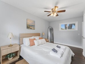 Ein Schlafzimmer mit einem Bett, Nachttischen, einem Deckenventilator, einem Fenster und einer Tür.