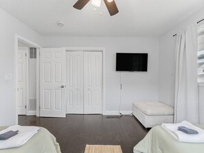 Une chambre avec deux lits, un ventilateur de plafond, un téléviseur à écran plat et une porte donnant sur une autre pièce.
