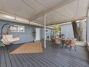 Une terrasse extérieure couverte comprenant un espace repas, des sièges et un fauteuil suspendu.