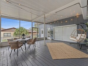 Eine Terrasse im Freien mit Tisch und Stühlen, einem Hängesessel und einem großen Fenster.