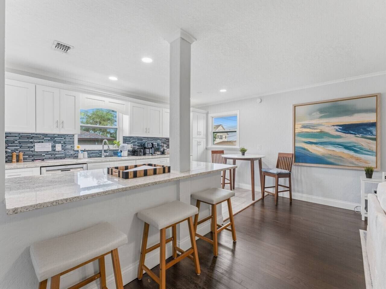 A modern kitchen with white cabinets, a central island with stools, and a dining area with a table and chairs.