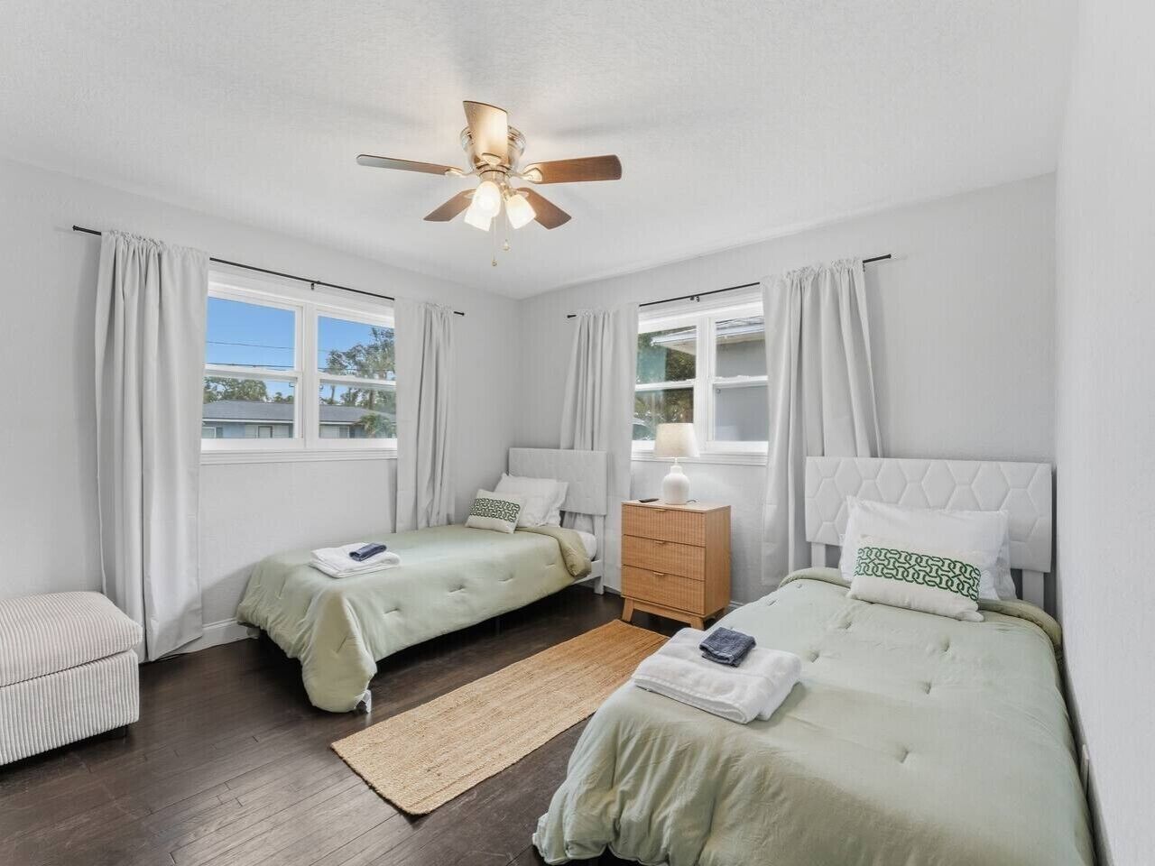 A bedroom with two beds, a ceiling fan, a nightstand, and a window with curtains.