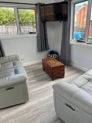 A room with a grey sofa, a wooden chest, and a television on the wall. - Cosy central guest house (Bellerive)