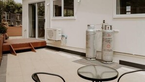 A modern building with a flat roof, large windows, and a patio area with outdoor seating. - Cosy central guest house (Bellerive)