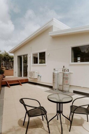 A modern building with a flat roof, large windows, and a patio area with outdoor seating. - Cosy central guest house (Bellerive)