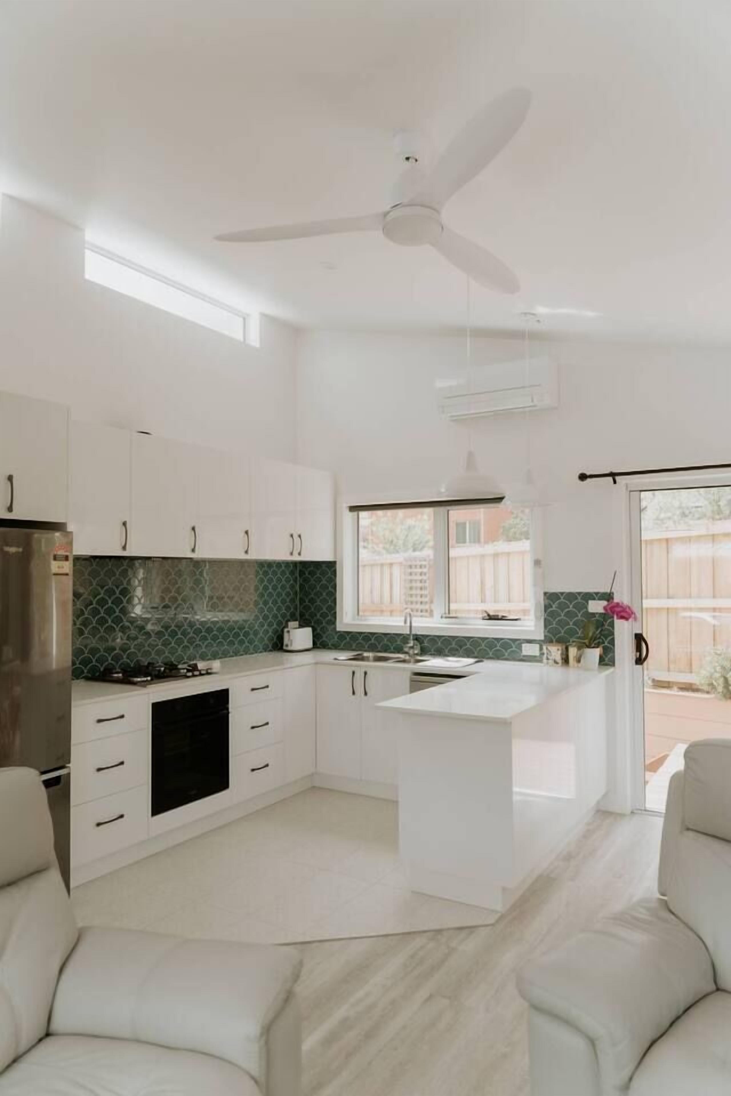 A modern kitchen with white cabinetry, a central island, and a ceiling fan.