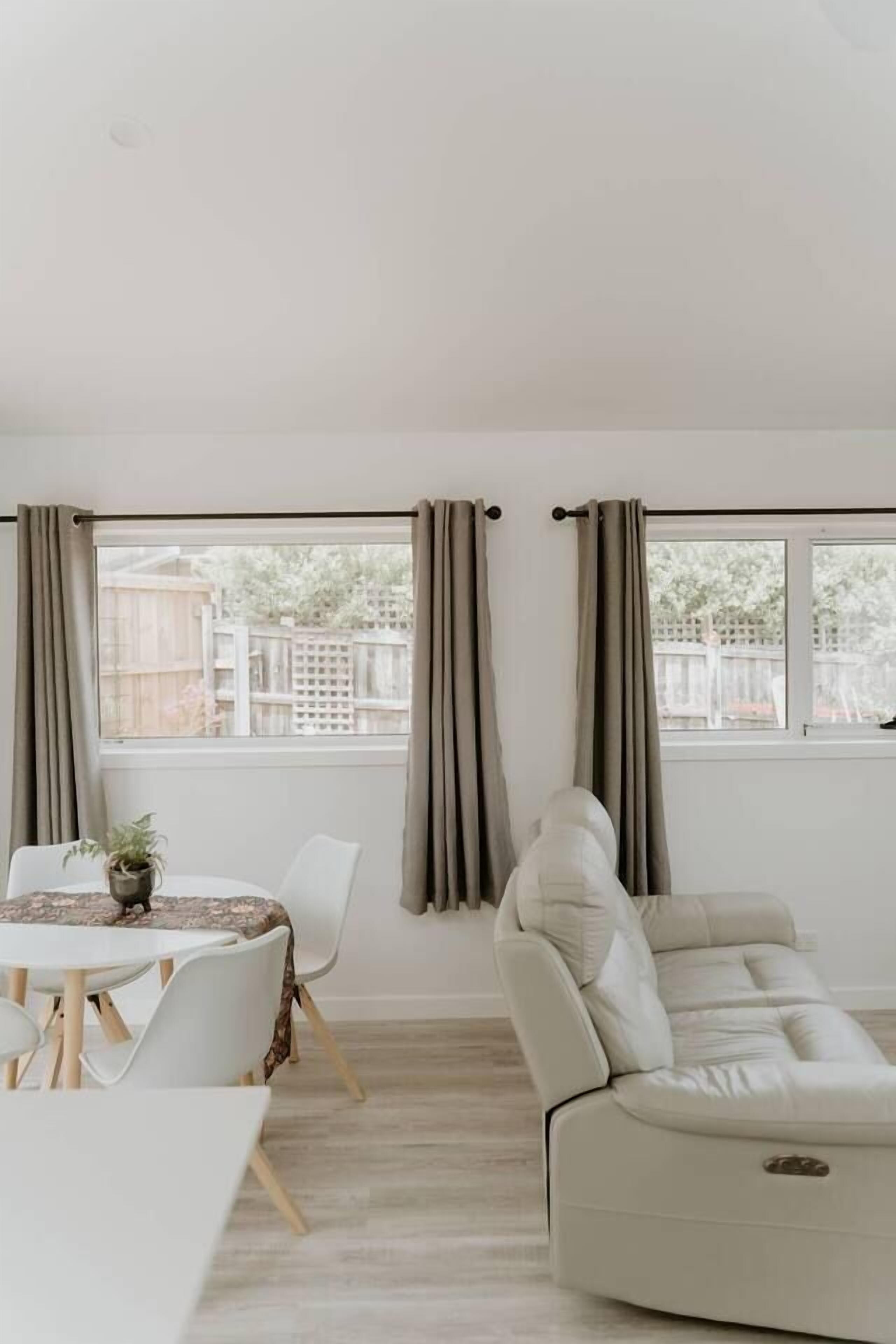 A modern living room with a sofa, a dining table with chairs, and a window with curtains.