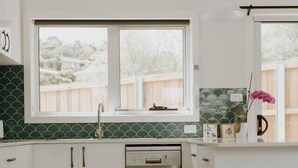 A kitchen with white cabinets, a dishwasher, a window, and a pendant light. - Cosy central guest house (Bellerive)