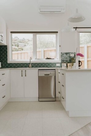 A kitchen with white cabinets, a dishwasher, a window, and a pendant light. - Cosy central guest house (Bellerive)