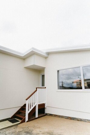 A corner of a building with a white exterior, a wooden staircase, and a large window reflecting the sky. - Cosy central guest house (Bellerive)