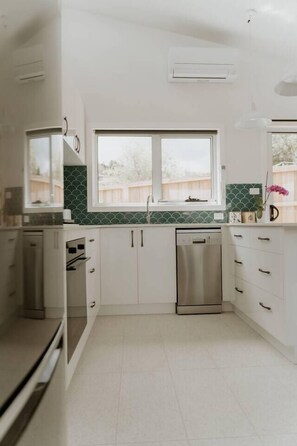 A kitchen with white cabinets, a stainless steel dishwasher, and a window above the sink. - Cosy central guest house (Bellerive)
