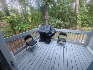 Eine Terrasse mit Grill und zwei Stühlen, umgeben von einem Wald.