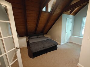 Ein Schlafzimmer mit schrägem Dach, einem Bett, einem Fenster und einer Tür.