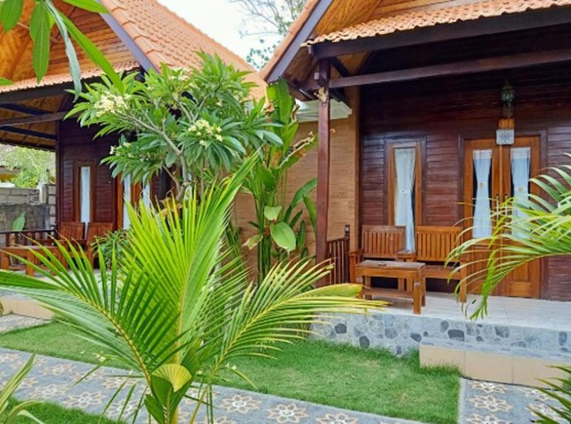 Uma cabana de madeira com varanda, mobiliário externo e plantas tropicais.