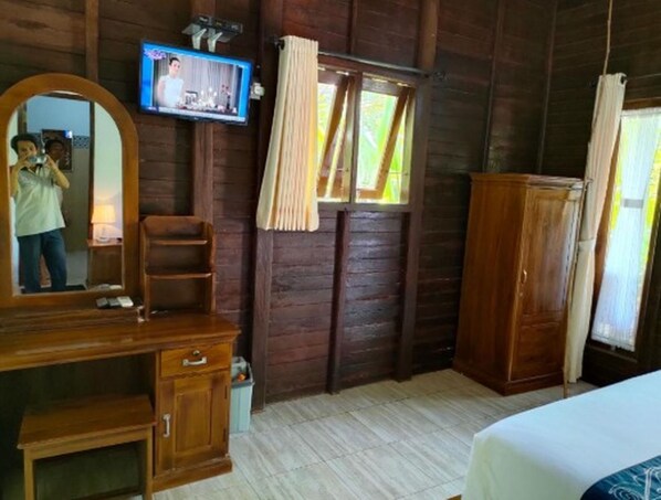 A wooden room with a bed, a dresser, a television mounted on the wall, and a window with curtains.