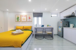 Habitación de hotel pequeña con cama, escritorio, dos sillas, refrigerador y ventana con cortina.