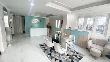 A modern hotel reception area with a glass desk, white chairs, and a geometric patterned rug.