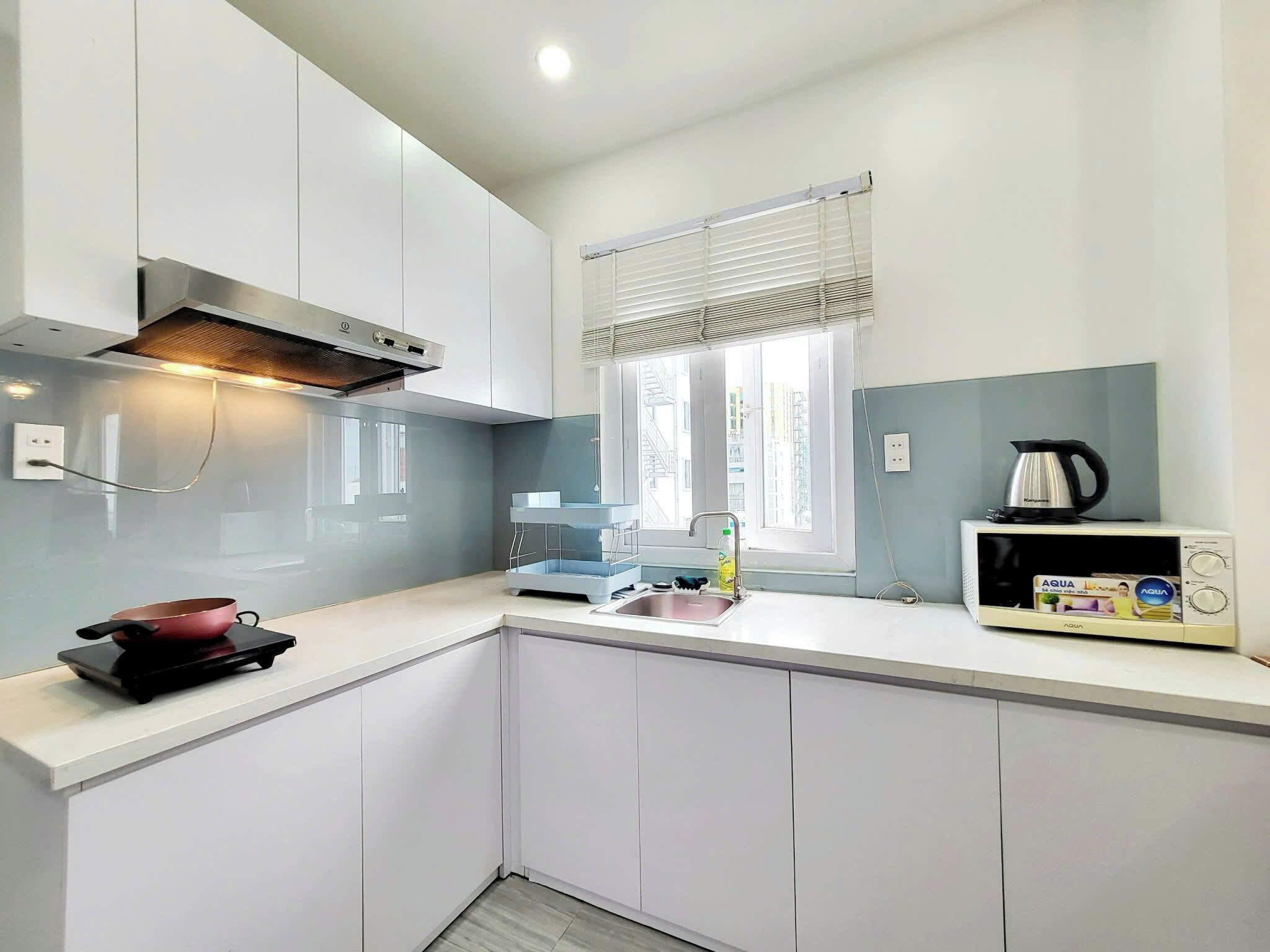 A modern kitchen with white cabinets, a built-in stove, a kettle, and a microwave.
