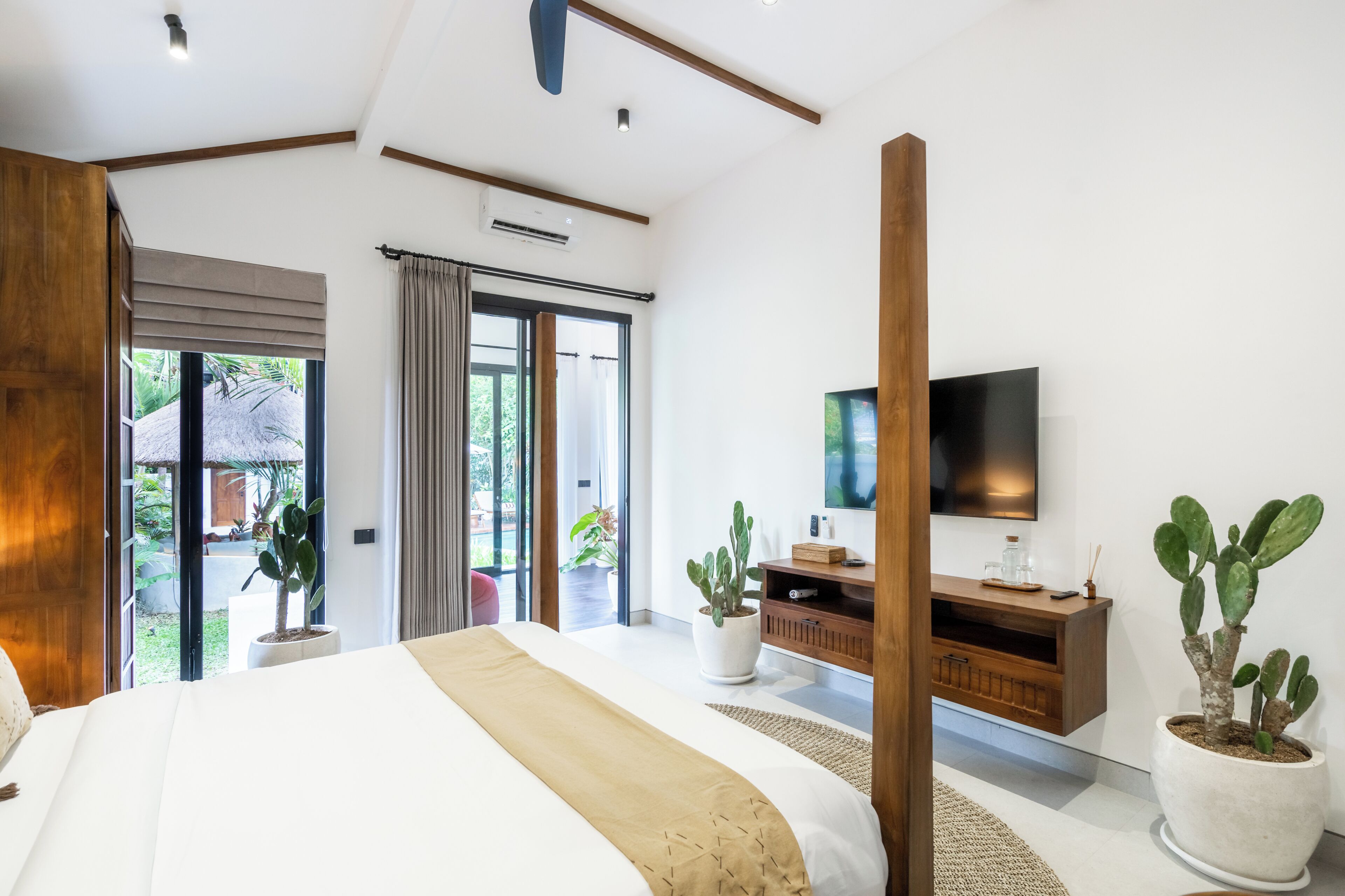 Un dormitorio moderno con una cama grande, un escritorio de madera, un televisor y plantas en macetas.