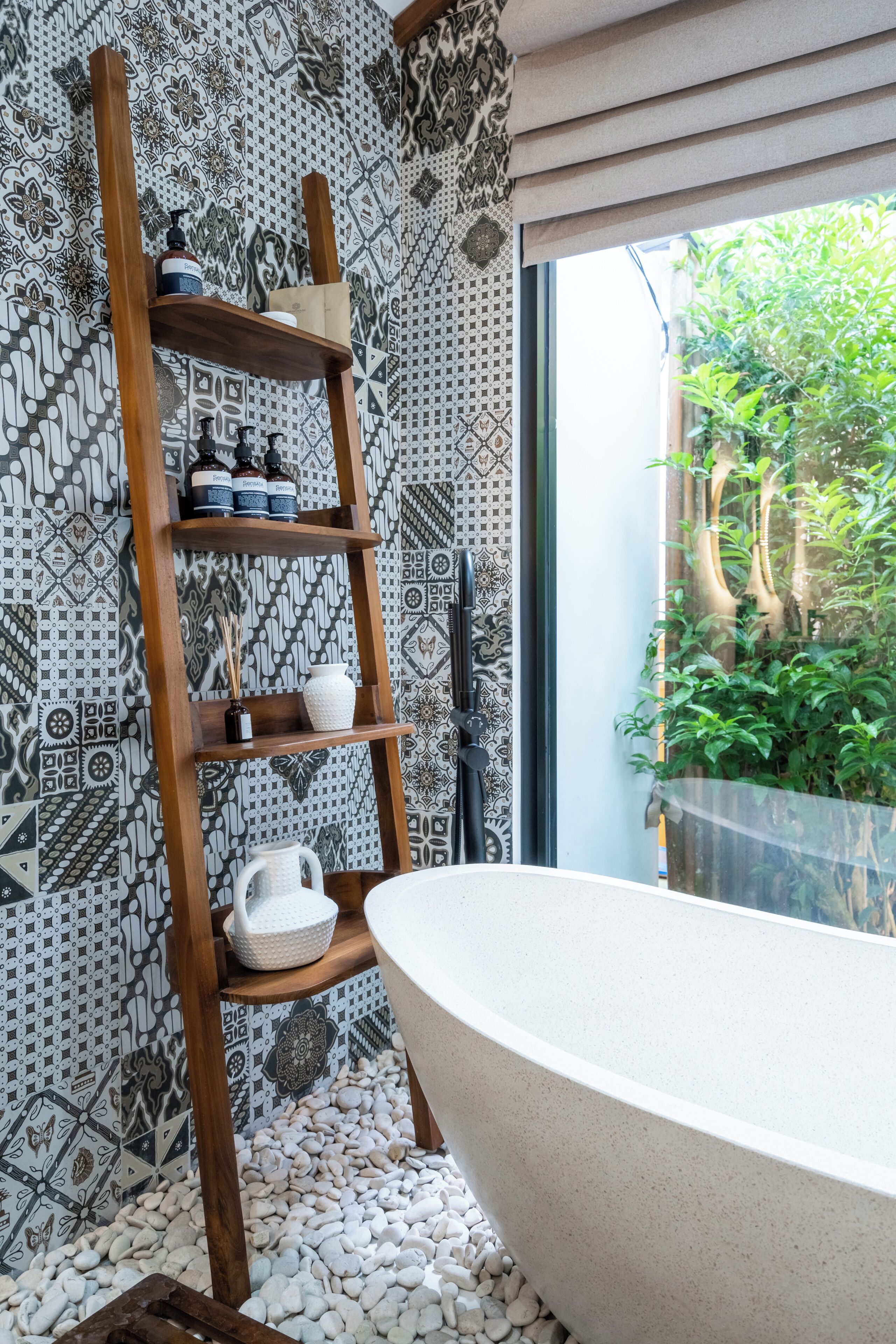 Baño con estante de madera tipo escalera para artículos de aseo, una bañera independiente y baldosas con diseño.