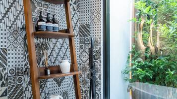 Baño con estante de madera tipo escalera para artículos de aseo, una bañera independiente y baldosas con diseño.