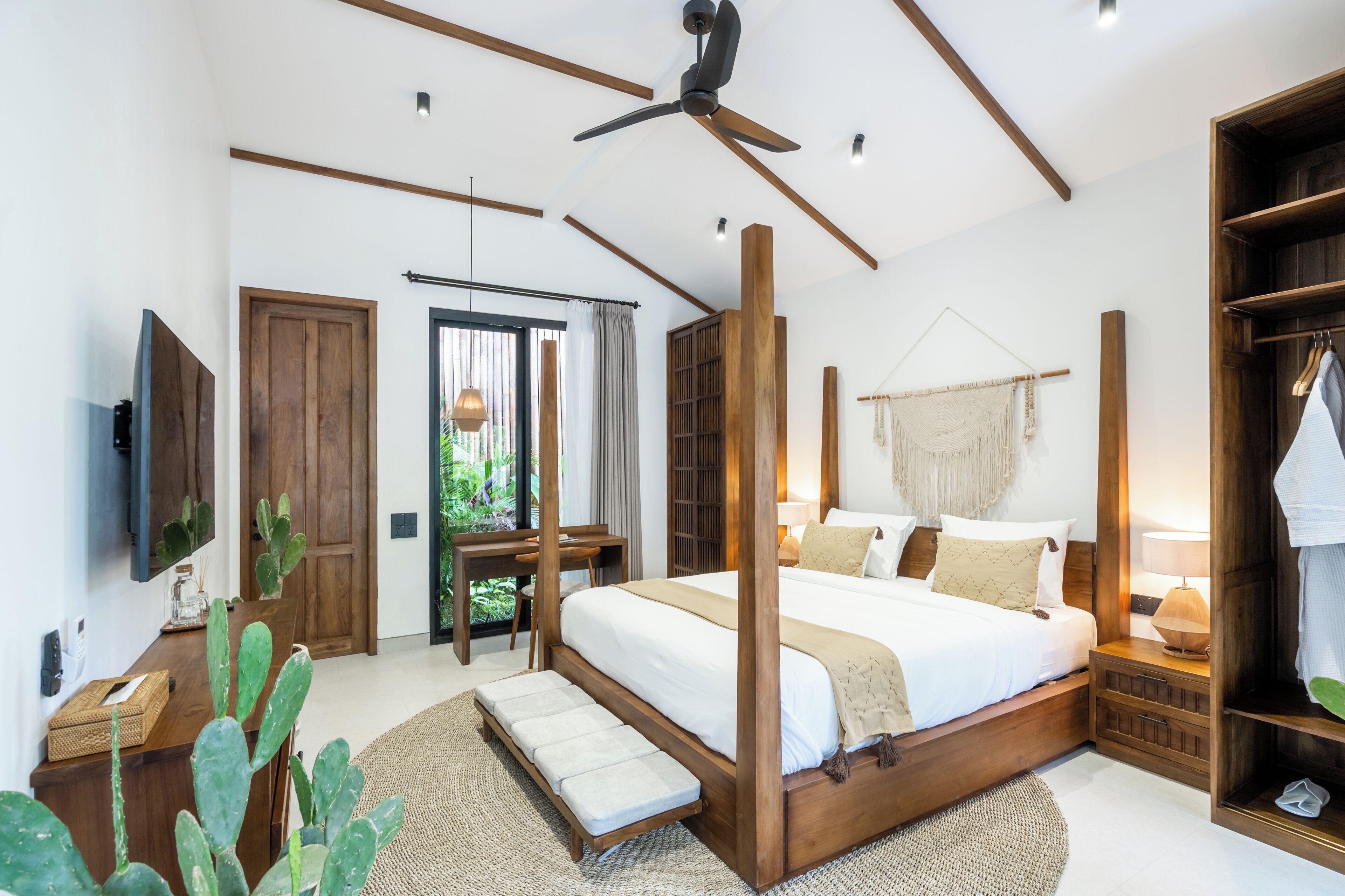 A bedroom with a four-poster bed, wooden beams, a ceiling fan, a TV, and a wardrobe.
