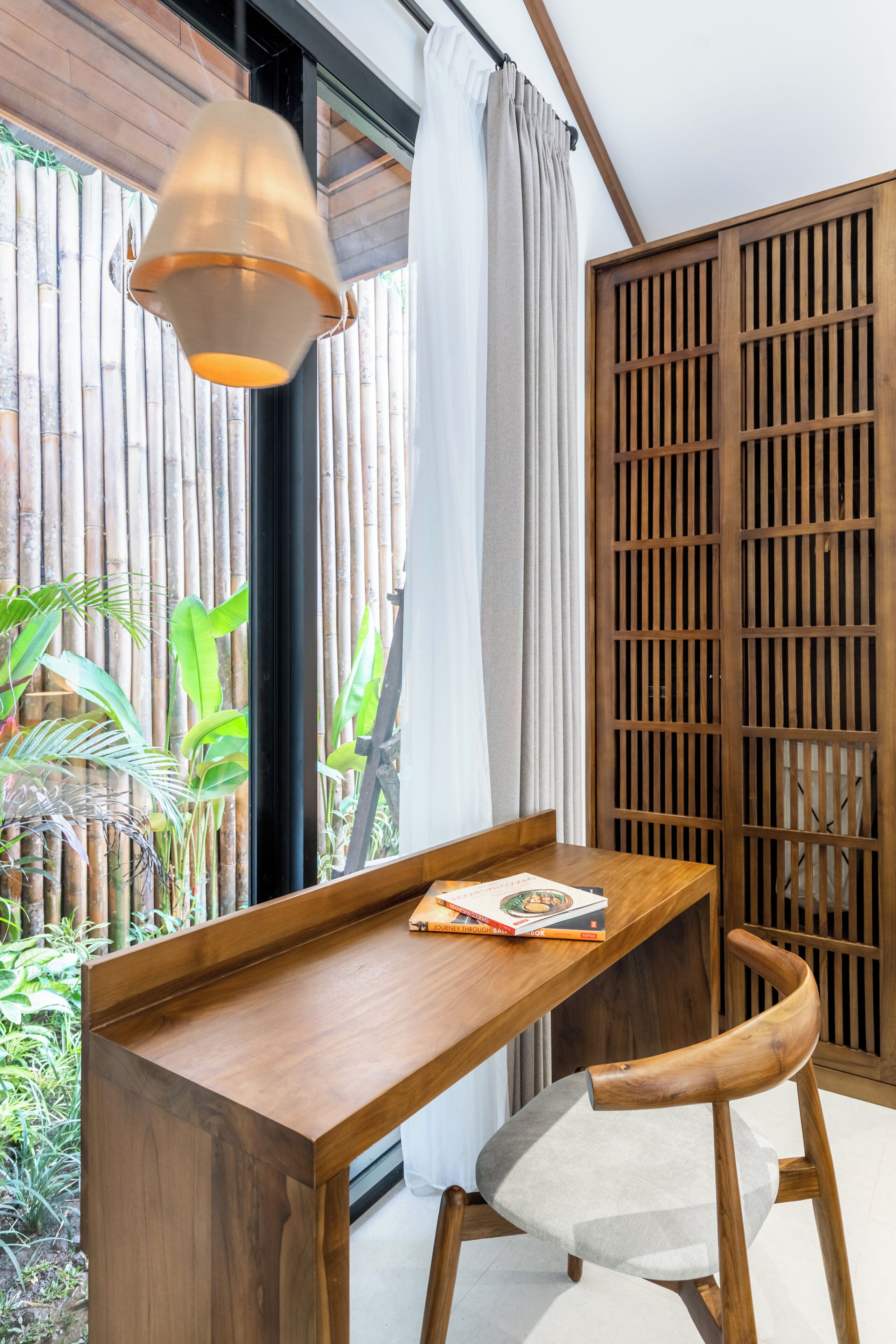 Una habitación con un escritorio de madera, una silla, una lámpara colgante, una cerca de bambú y una puerta corredera.