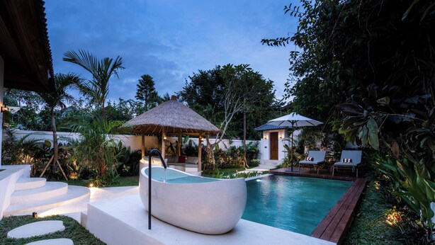 Un área de piscina moderna al aire libre con un jacuzzi, sillas de descanso y una estructura de techo de paja.