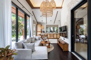 A modern living room with a sectional sofa, a dining area, and a kitchen. - Capri Villa by DH (Gianyar)