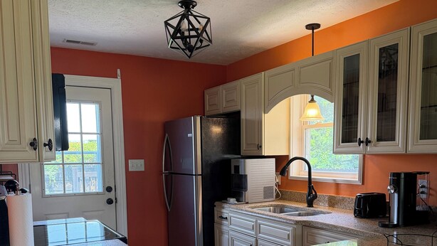 A kitchen with white cabinets, a stainless steel refrigerator, a granite countertop, and a window with a view of greenery.