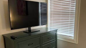 A room with a television on a cabinet, a window with blinds, and a remote control on the cabinet.