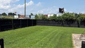 A well-maintained grassy backyard with a wooden fence, a utility pole, and commercial buildings in the background.