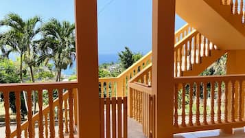 A spacious indoor area with a tiled floor, a staircase with a balustrade, and a view of palm trees and buildings through a window.