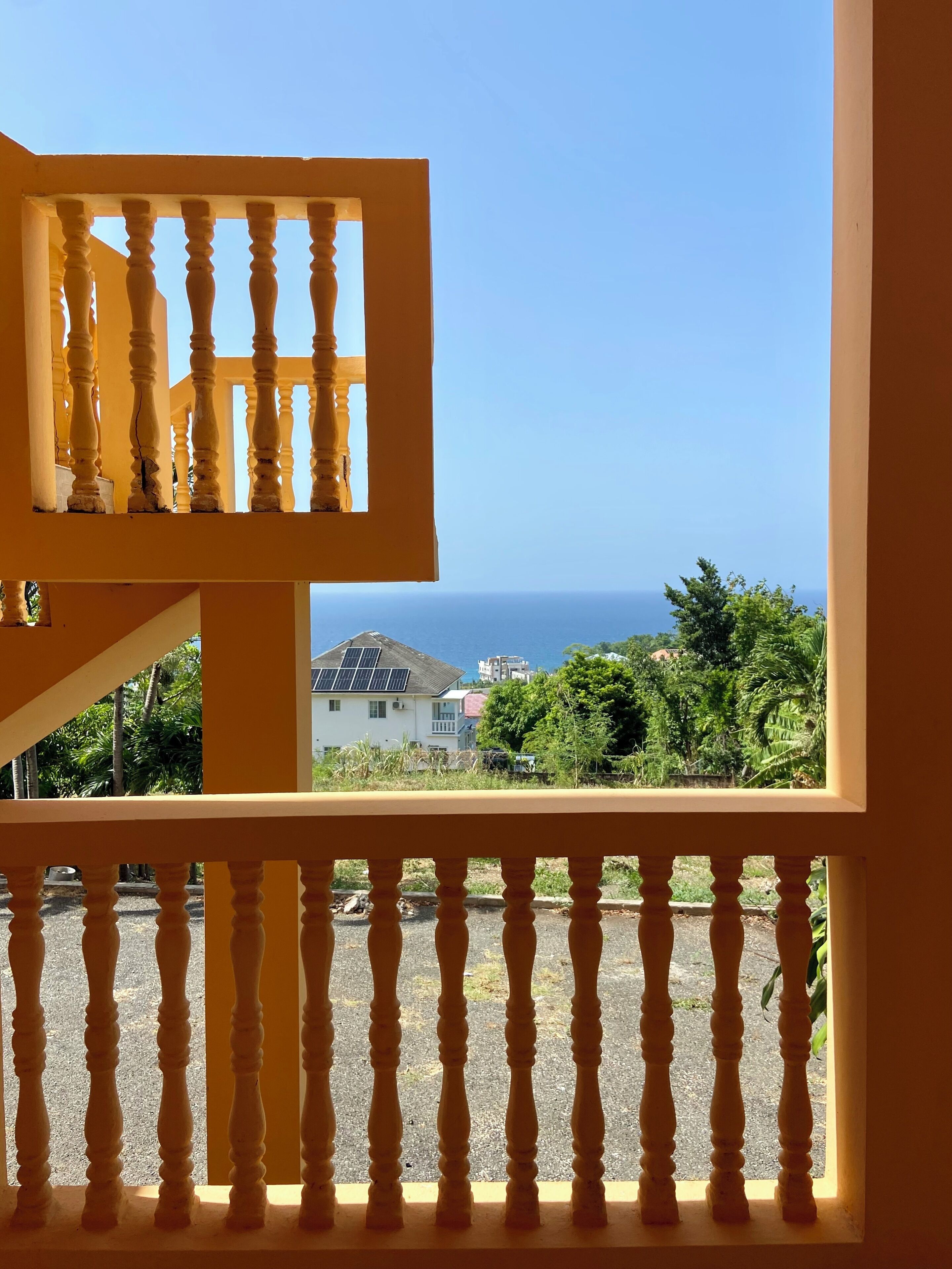 A balcony with a view of the sea and surrounding greenery.